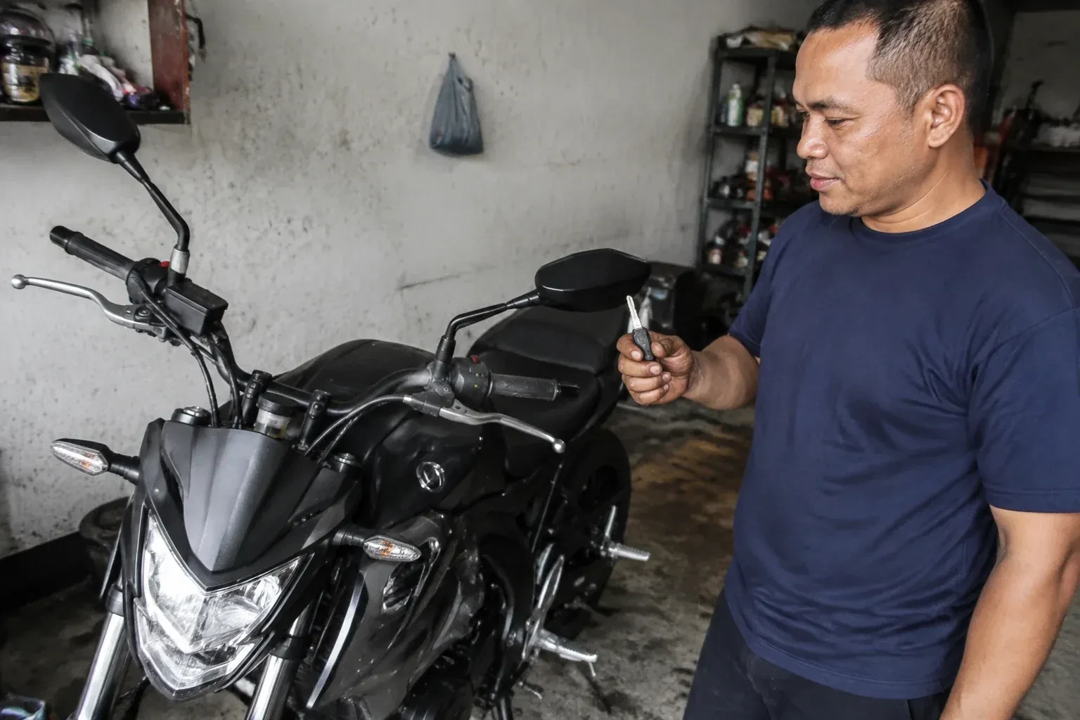 Person holding a key beside a black motorcycle in a garage. — Motorcycle & Scooter Keys, Vellore