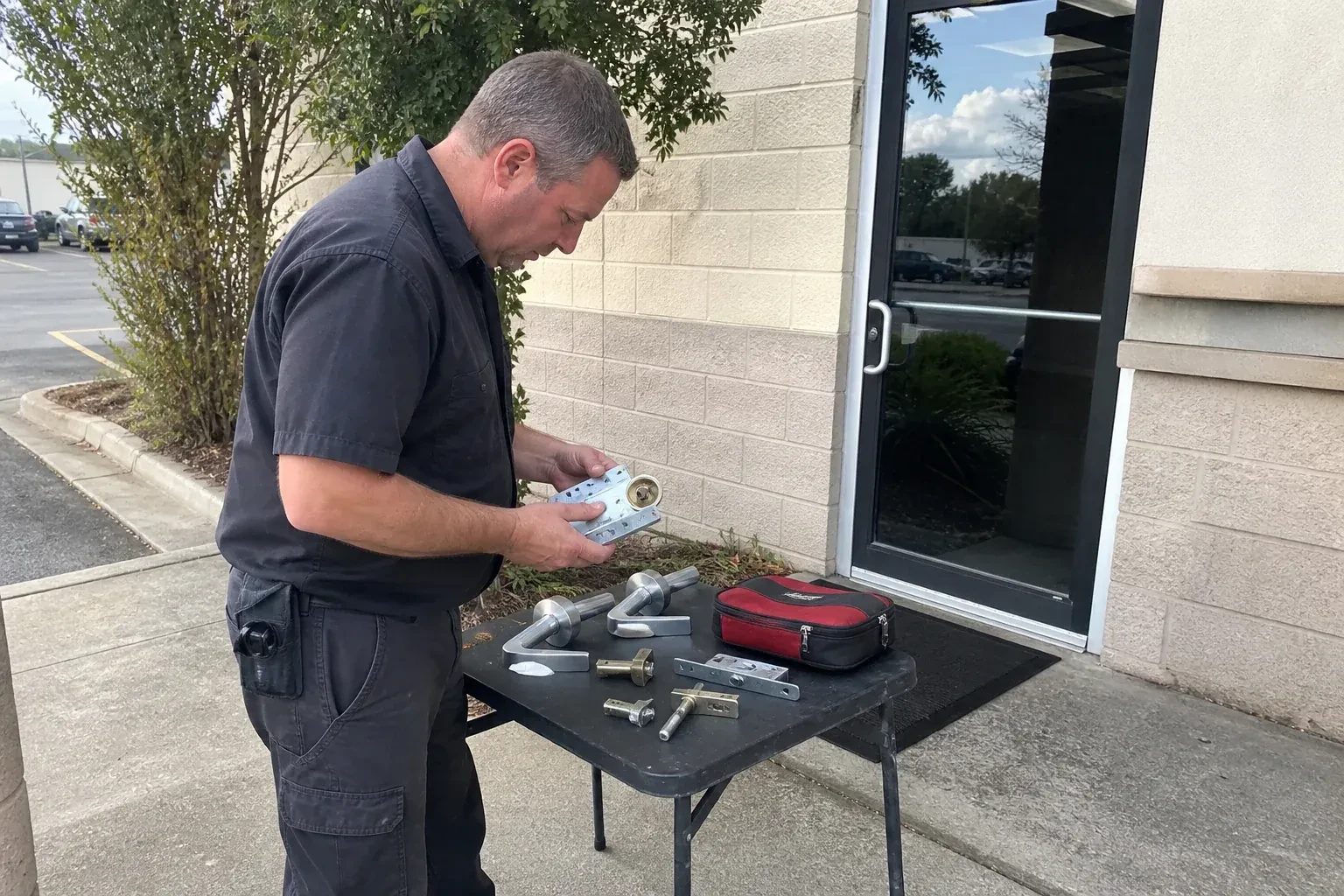 Technician examining detached commercial lock hardware on a table outside a shop entrance. — Business Lockout Service, Vaughan